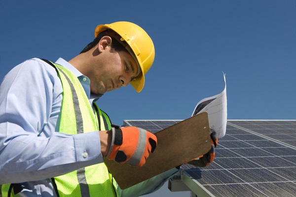 Side view of young maintenance worker looking at clipboard near solar panels